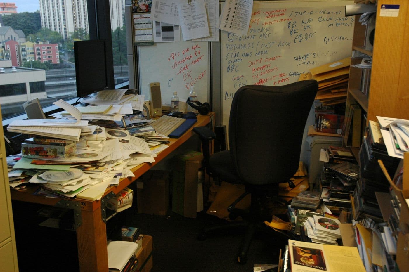 A desk buried in paperwork, with notes scrawled across a whiteboard behind it